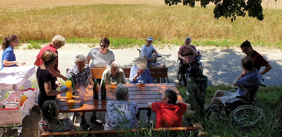 BewohnerInnen sitzen draußen im Schatten.